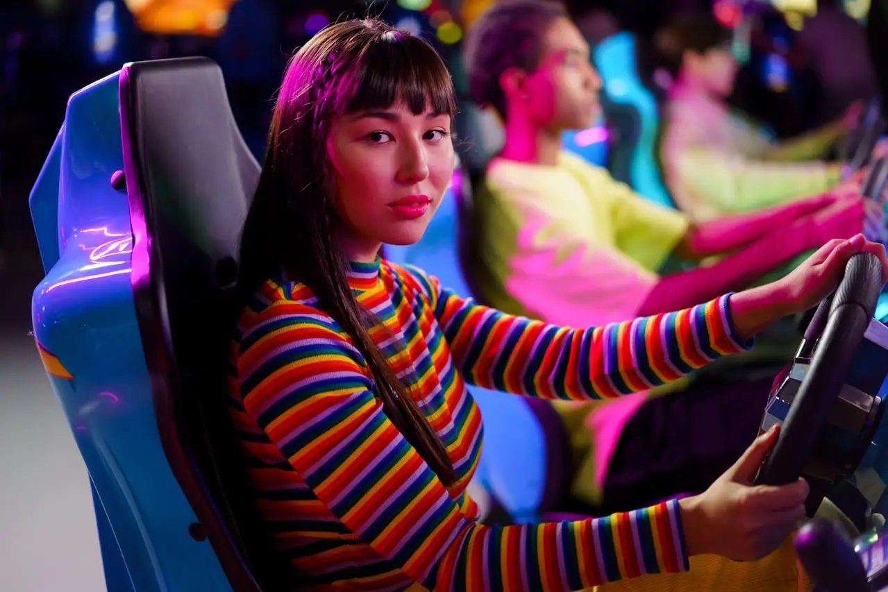 Young woman in a colorful striped sweater playing an arcade racing game, focused and illuminated by neon lights.