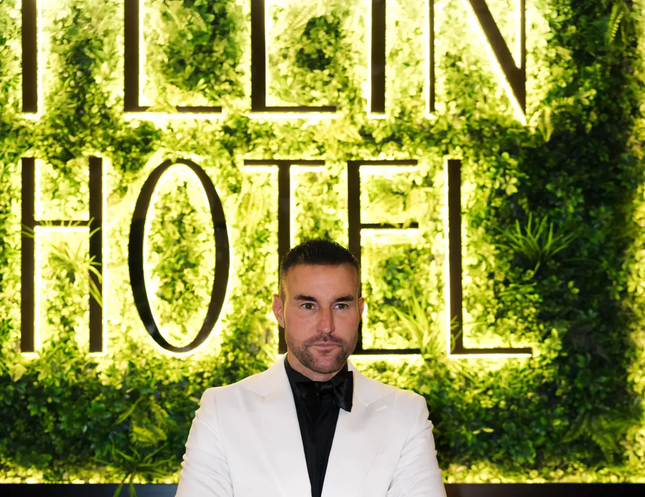 Albania To Welcome Philipp Plein’s First Signature Hotel And Dining Venue 2 Philipp Plein in front of a green and gold sign that reads “PLEIN HOTEL” at a luxury venue.