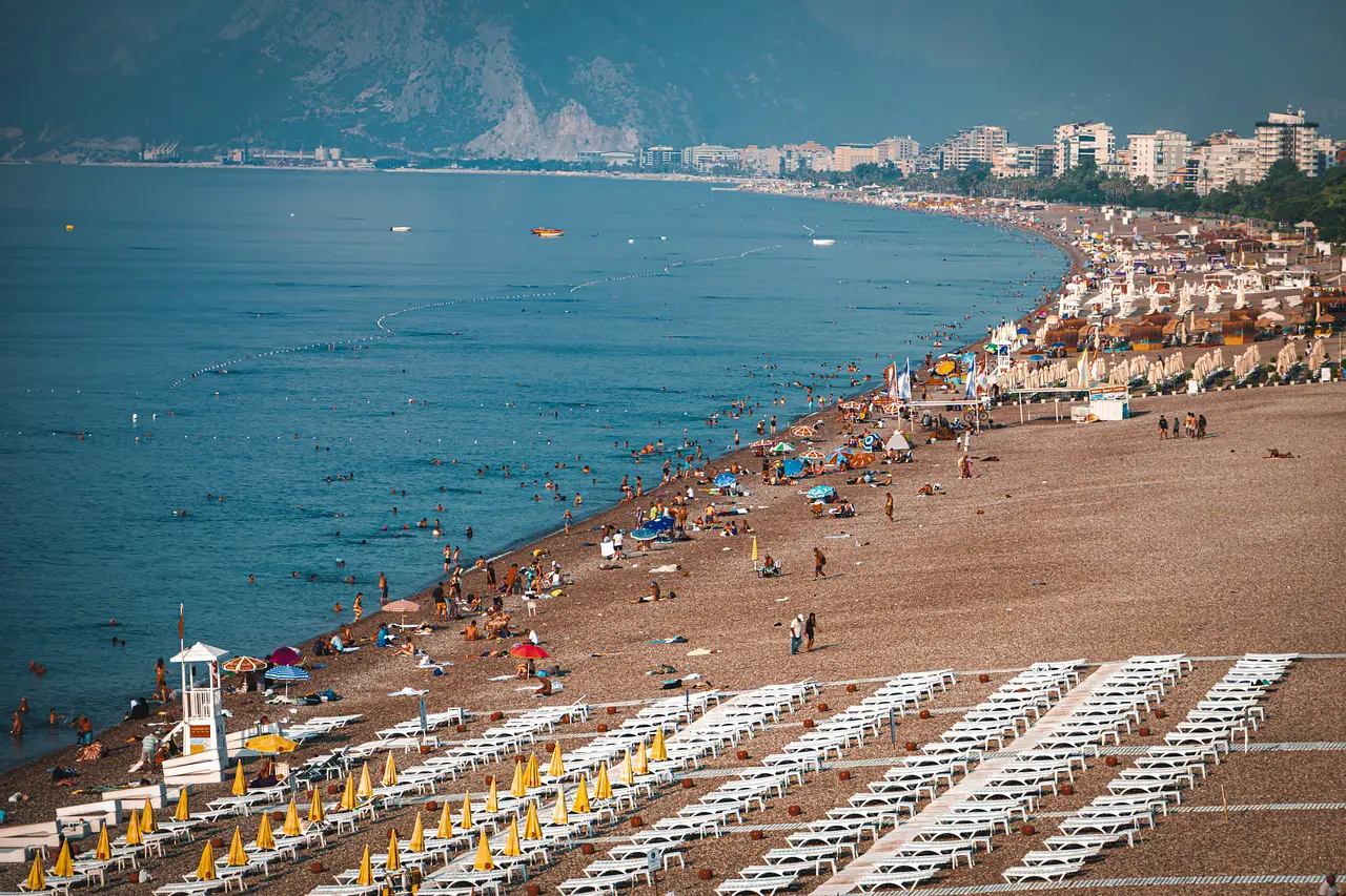 Las animadas playas de Antalya están llenas de tumbonas y sombrillas mientras los turistas disfrutan de las aguas turquesas y las hermosas vistas de la costa.