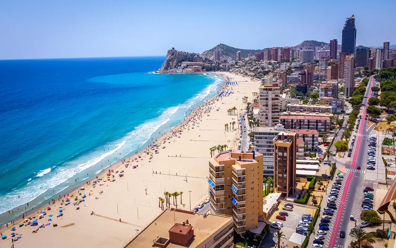 Aerial view of Benidorm’s beach with turquoise waters, golden sand, and high-rise hotels lining the coast.