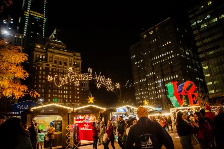 Festive Christmas Village in Philadelphia at night with holiday market stalls and the iconic “LOVE” sculpture nearby.