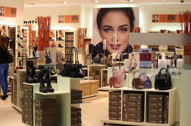 An interior view of a stylish retail store displays handbags, boots, and shoe boxes, with a large promotional poster of a woman in the background.