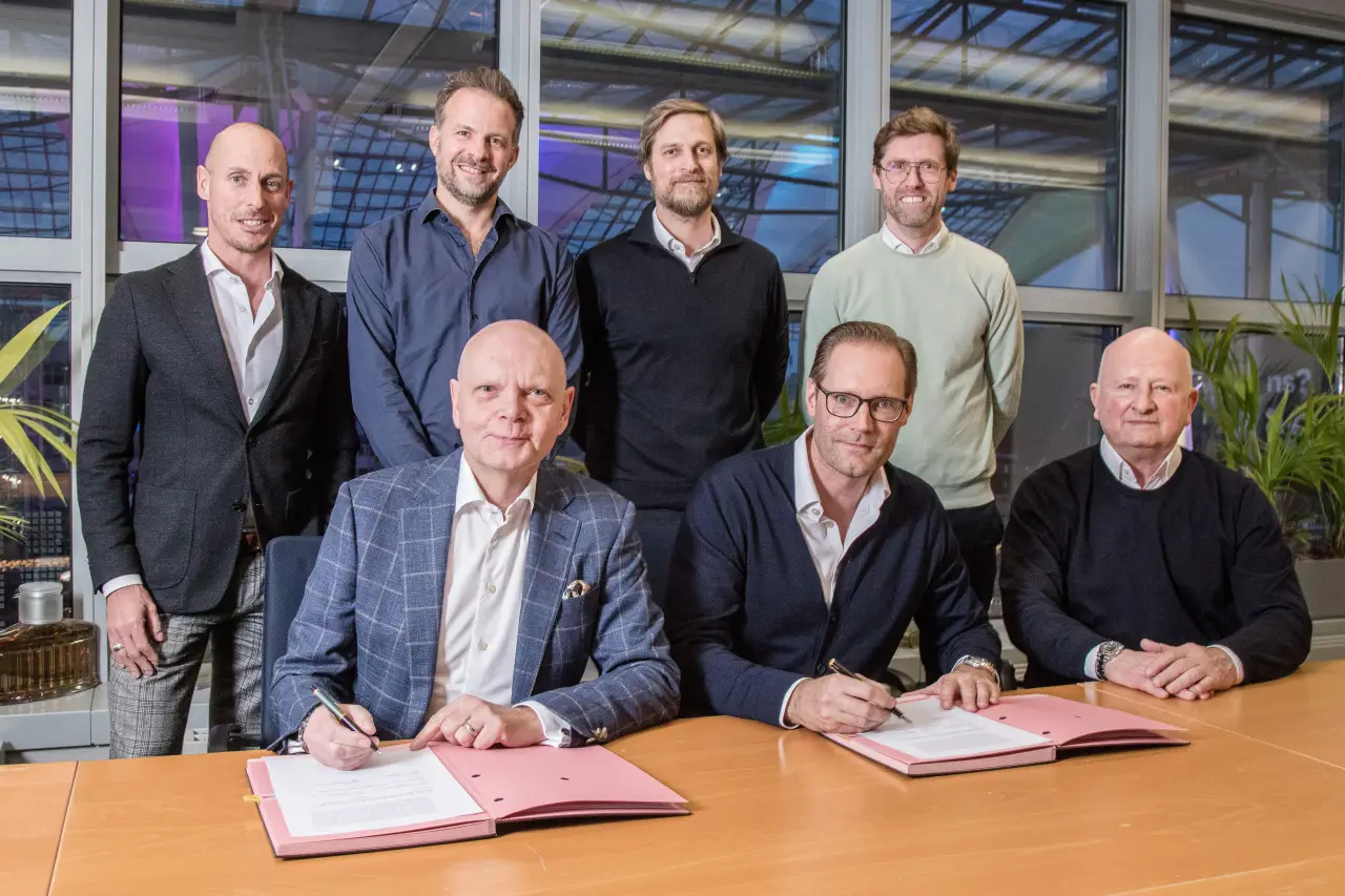 Seven executives from Gebr. Heinemann and eurotrade pose during a contract signing ceremony at Munich Airport, with two signing documents at the table.