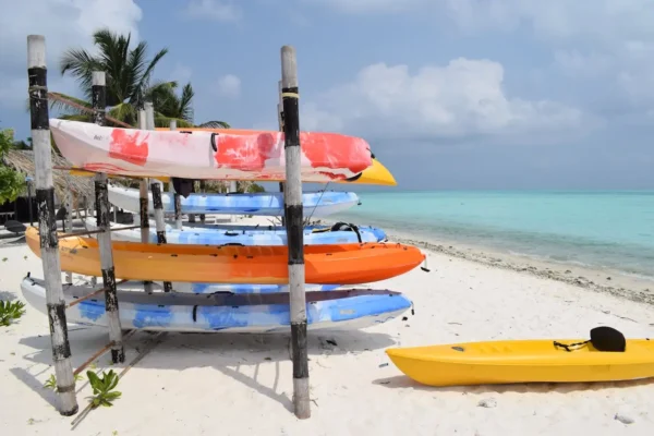 Colorful kayaks stacked on a wooden rack by a white sandy beach in Lakshadweep, with turquoise waters and a clear sky in the background.