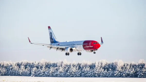 A Norwegian Air aircraft landing on a snow-covered runway, surrounded by frosty trees.