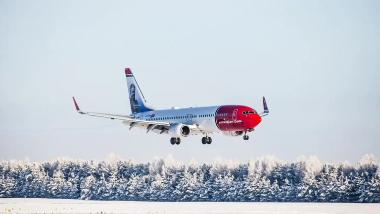 A Norwegian Air aircraft landing on a snow-covered runway, surrounded by frosty trees.