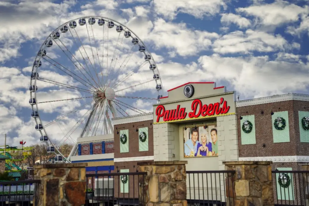 The iconic Ferris wheel at The Island in Pigeon Forge rises behind Paula Deen’s Family Kitchen. Under a cloudy sky, it is adorned with festive holiday wreaths.