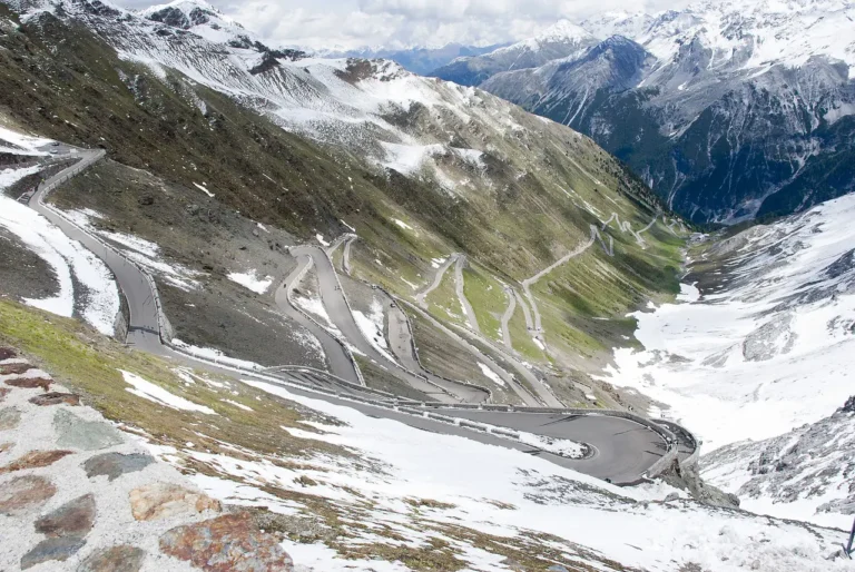 A winding mountain road of the Stelvio Pass in Italy, surrounded by snow-capped peaks and rugged alpine scenery.