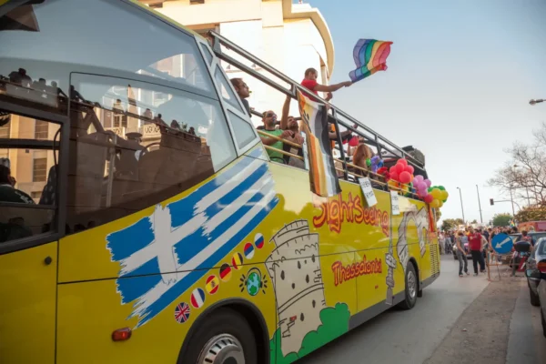 Colorful open-top sightseeing bus with Greek and rainbow flags during Thessaloniki Pride.