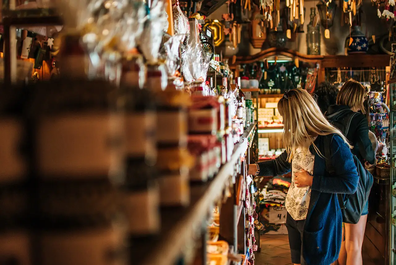 Surprises In Travel Shopping: Adding Adventure To Every Purchase 2 Travelers engaged in travel shopping at a local market filled with unique souvenirs and handmade goods.