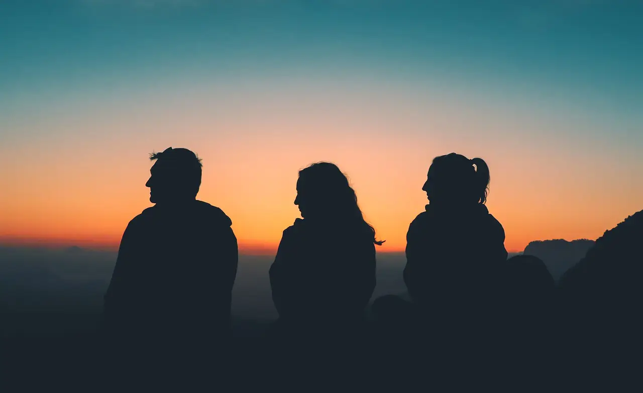 Silhouettes of three travelers enjoying a scenic sunset view over the mountains.