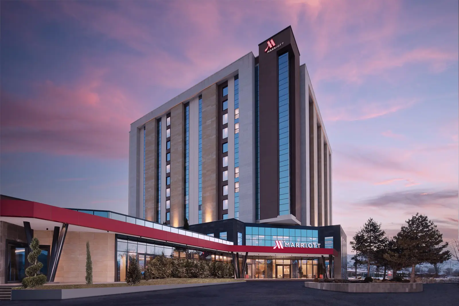 Exterior view of the Cappadocia Marriott Hotel at sunset, showcasing its modern architectural design and illuminated façade against a colorful sky.