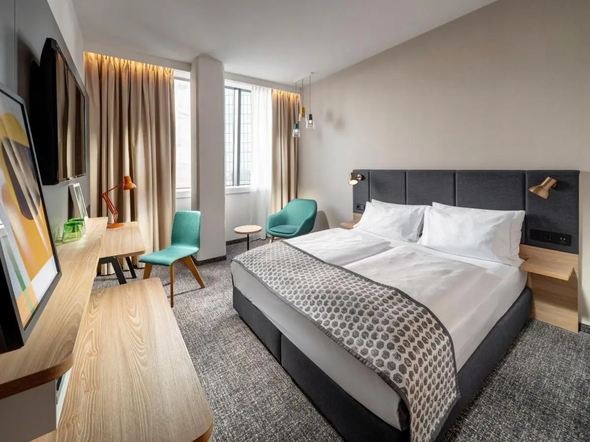 Modern hotel room with a double bed, stylish furniture, and large windows.