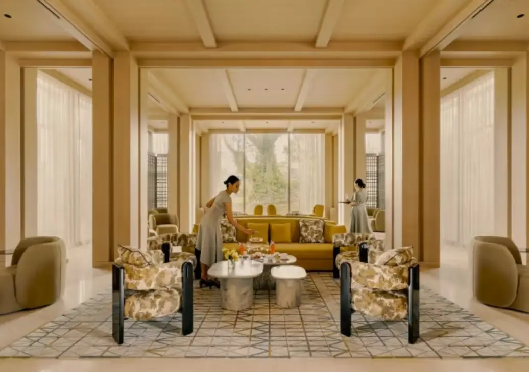 Elegant lounge interior with floral-patterned chairs and a contemporary table set for high tea, with staff attending to guests in a serene ambiance.