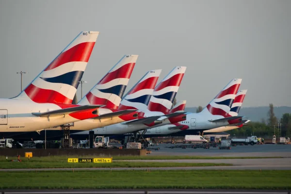 Row of British Airways planes lined up at the airport with their tail fins visible.