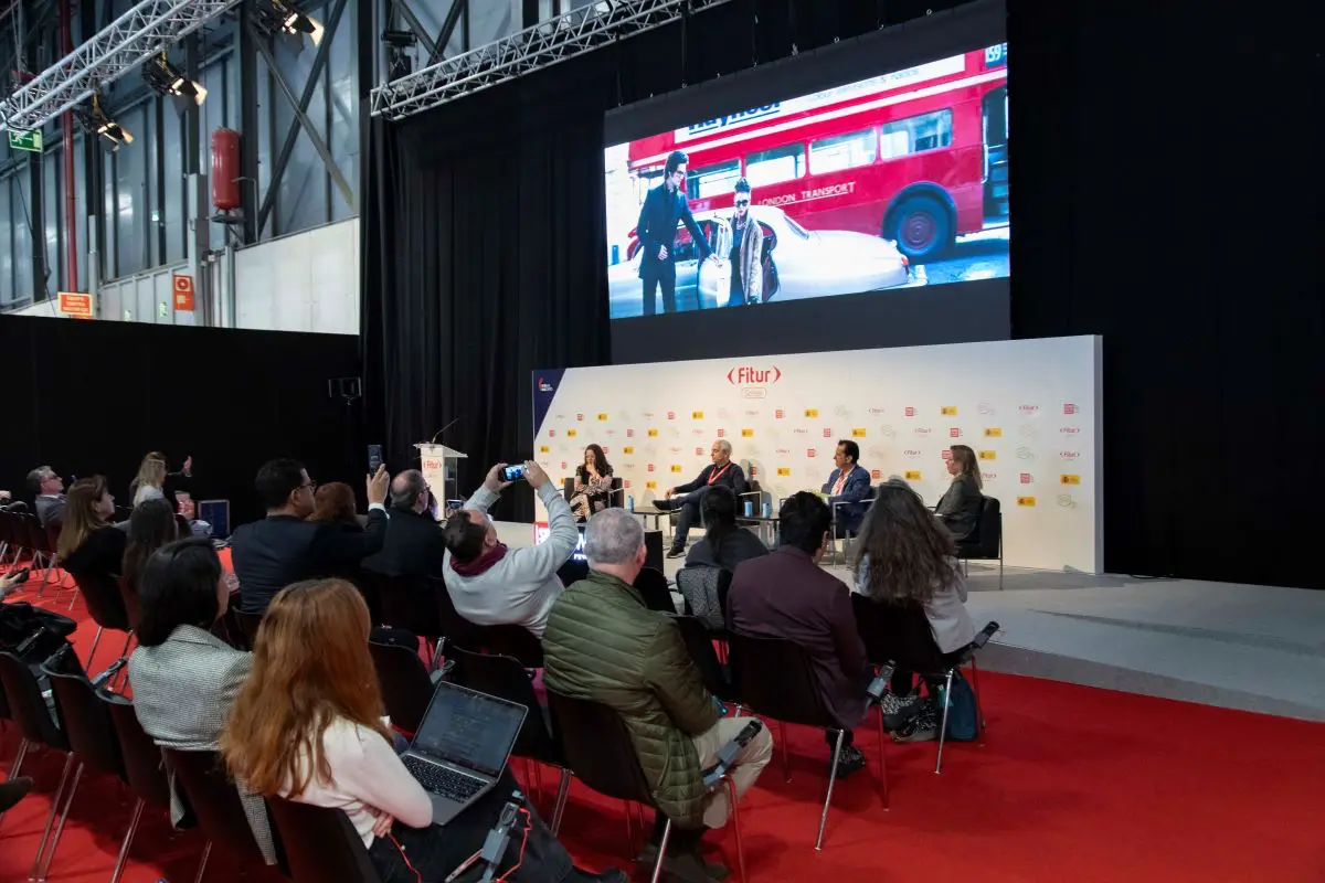 A panel discussion at FITUR Screen with an audience watching and a large screen displaying a film scene.