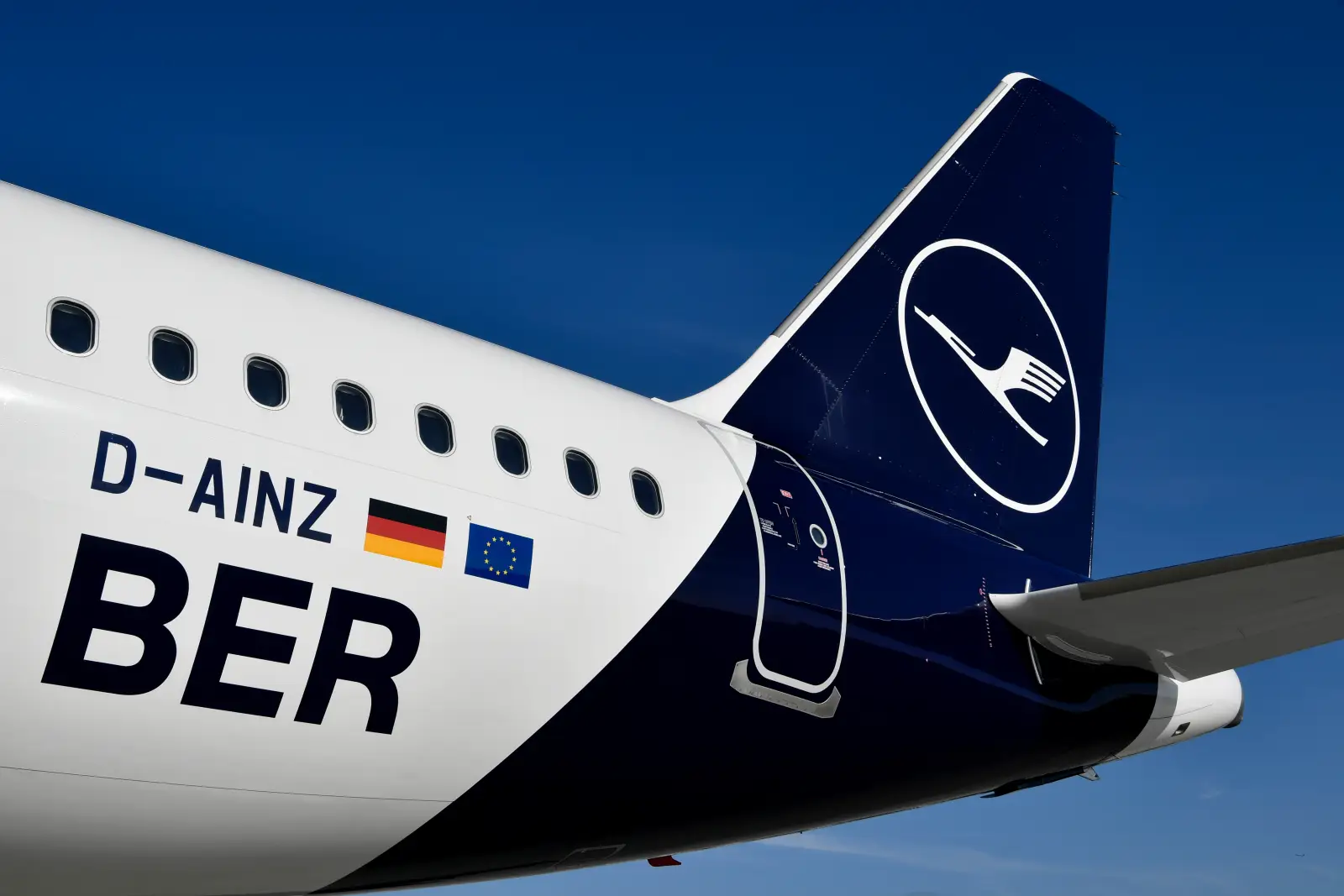 Lufthansa aircraft with “BER” designation and logo on the tail against a blue sky.