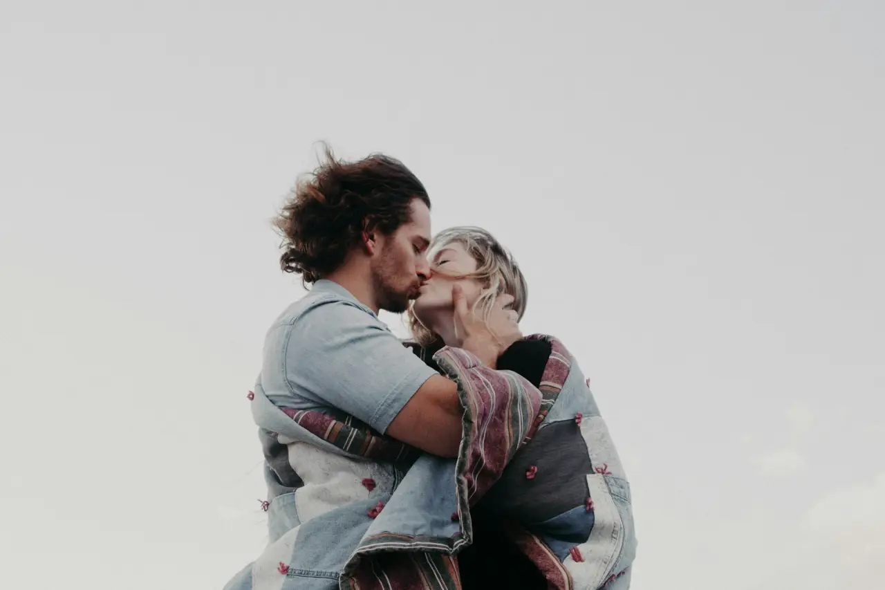 Romantic couple sharing a kiss wrapped in a cozy blanket under a clear sky.