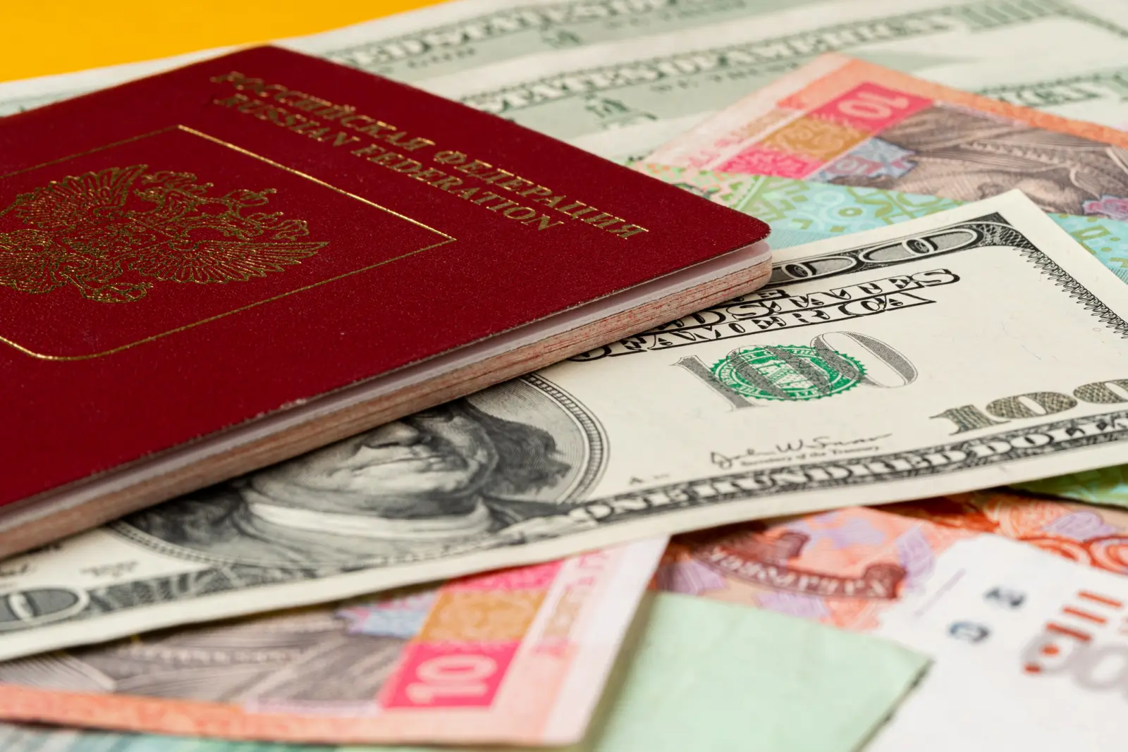 How Can Russian Tourists Pay Abroad In 2025? 2 A Russian passport placed on top of U.S. dollar bills and various international banknotes.