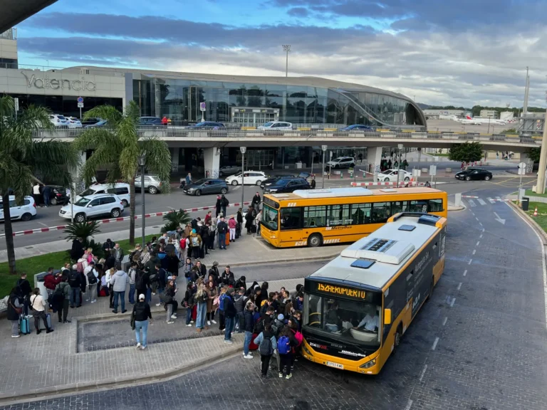Crowds of travelers waiting near yellow buses outside Valencia Airport on a busy day.