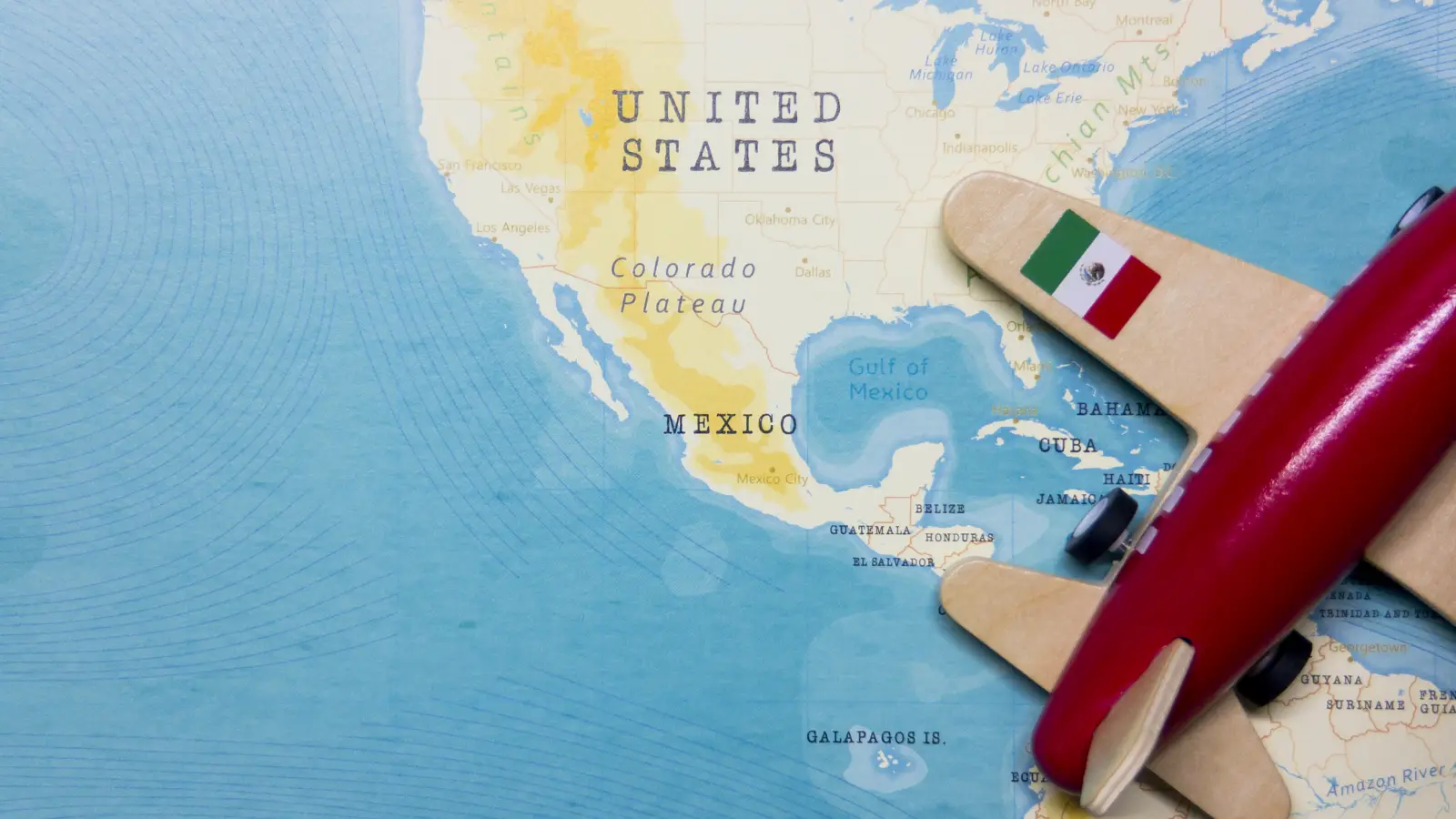 Toy airplane with a Mexican flag wing over a map of the U.S. and Mexico, symbolizing the best airlines to fly to Mexico.