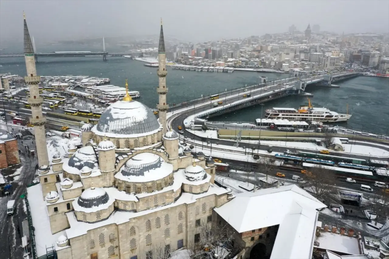 Aerial view of Istanbul covered in snow, featuring a historic mosque and the Galata Bridge.