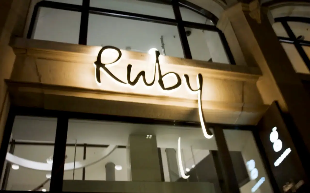 Illuminated Ruby Hotels logo sign on a building exterior at night.