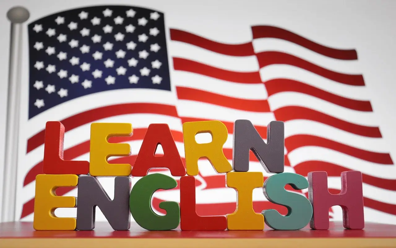 Colorful wooden letters spelling “Learn English” with an American flag in the background.