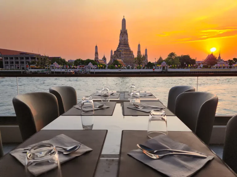 Luxury river cruise dining in Bangkok with a sunset view of Wat Arun.