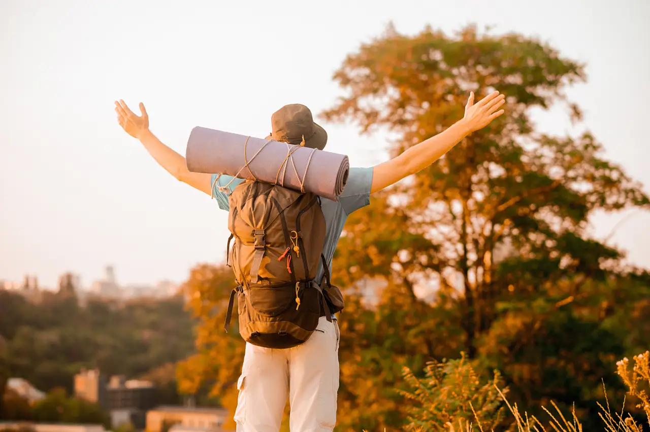 Traveler with backpack and yoga mat enjoying nature with open arms.