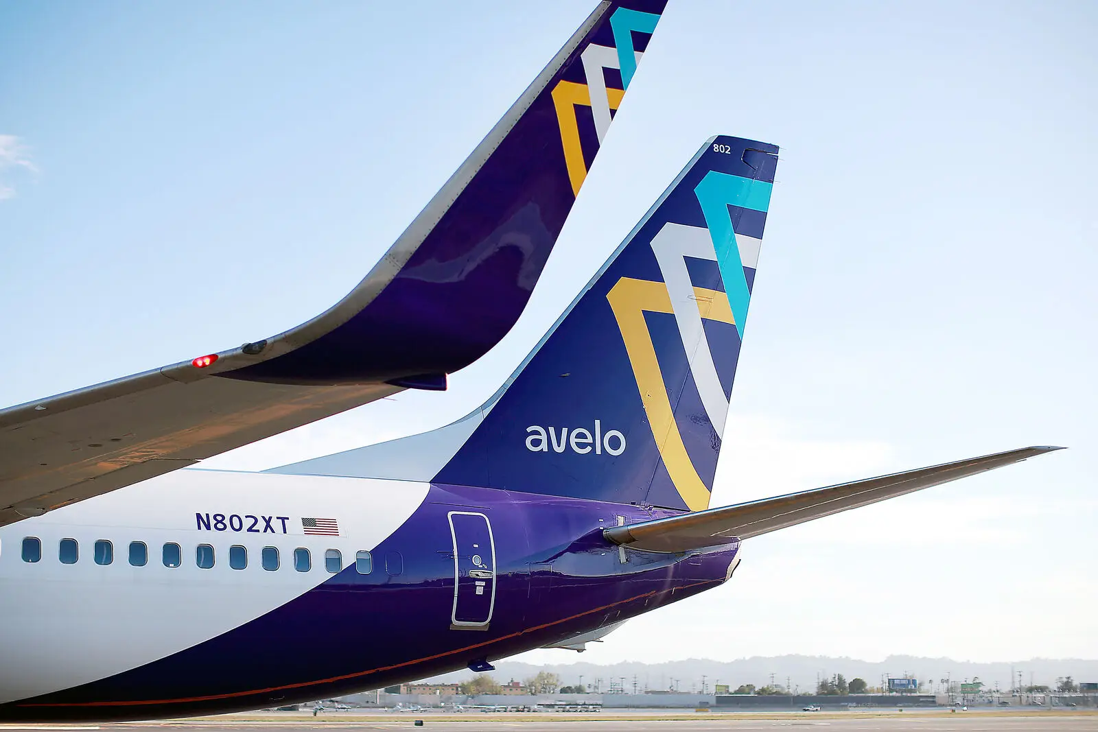 A close-up of two Avelo Airlines Boeing 737 aircraft tails featuring the airline’s signature purple, blue, and gold livery.