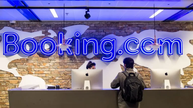 A customer at the Booking.com office reception desk with a neon-lit logo in the background.