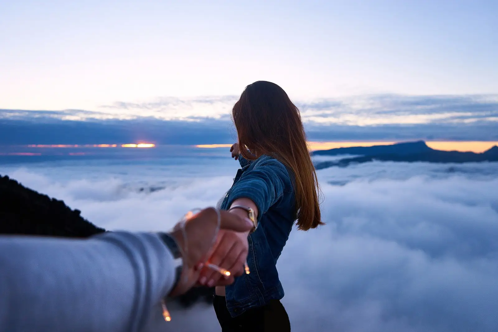 A couple holding hands on a mountain above the clouds at sunrise, symbolizing adventure and travel romance.