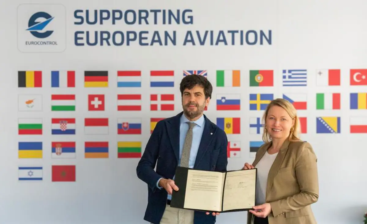 EUROCONTROL and EUROCAE representatives hold a signed agreement in front of a backdrop displaying European country flags and the EUROCONTROL logo.