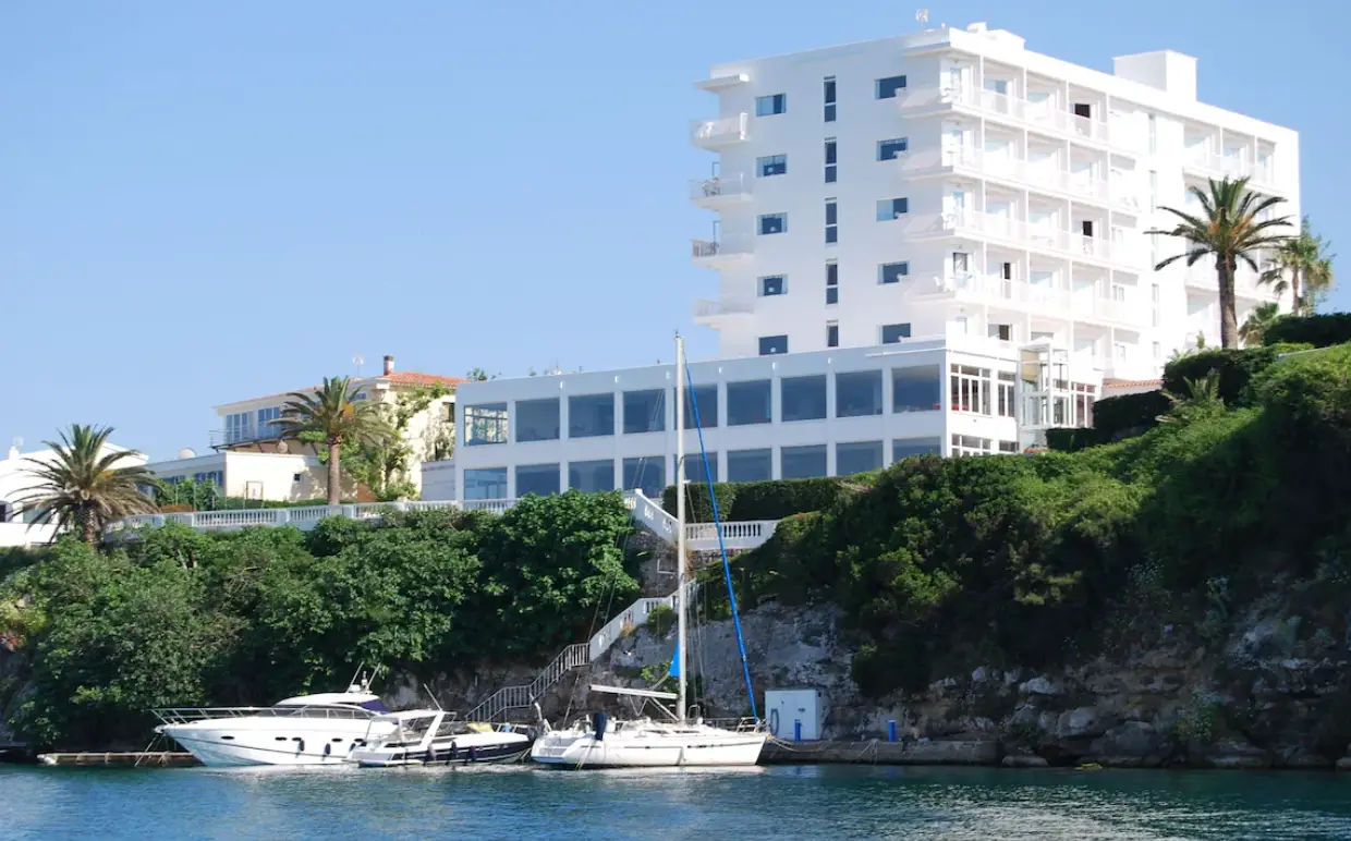 Hotel Indigo Menorca overlooking the sea with boats docked nearby, surrounded by lush greenery.