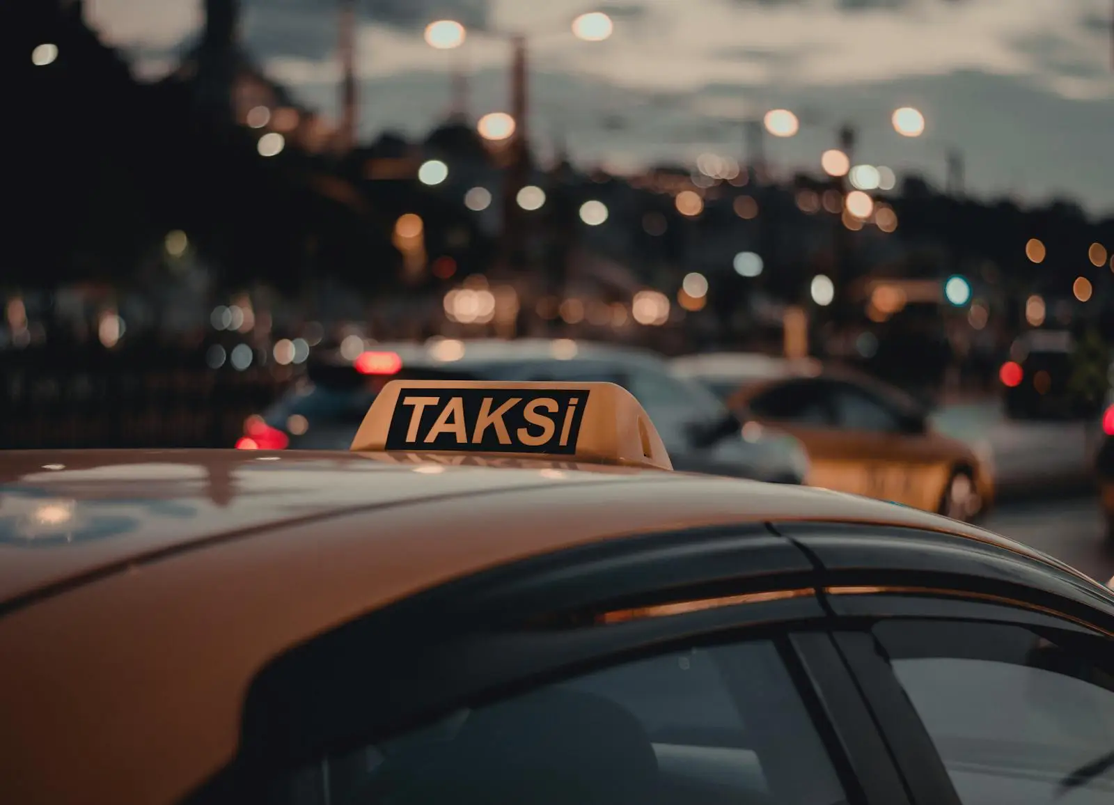 A yellow taxi in Istanbul with a “TAKSİ” sign on top, captured at night with blurred city lights and traffic in the background.