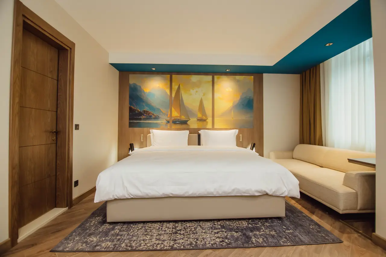 Modern hotel room with a large bed, scenic sailboat artwork, and natural light in Batumi