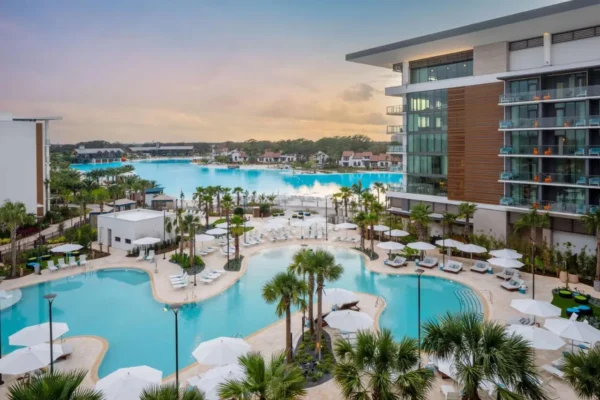 View of the Conrad Orlando resort’s lagoon-style pool with palm trees, sun loungers, and a luxury tower overlooking Evermore Bay.