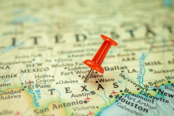 A close-up of a map of Texas with a red pushpin marking a location near Austin, highlighting major cities and travel routes.
