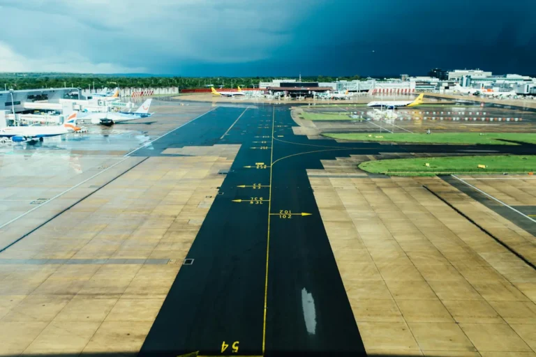 A wet airport runway with multiple parked airplanes and a stormy sky in the background.
