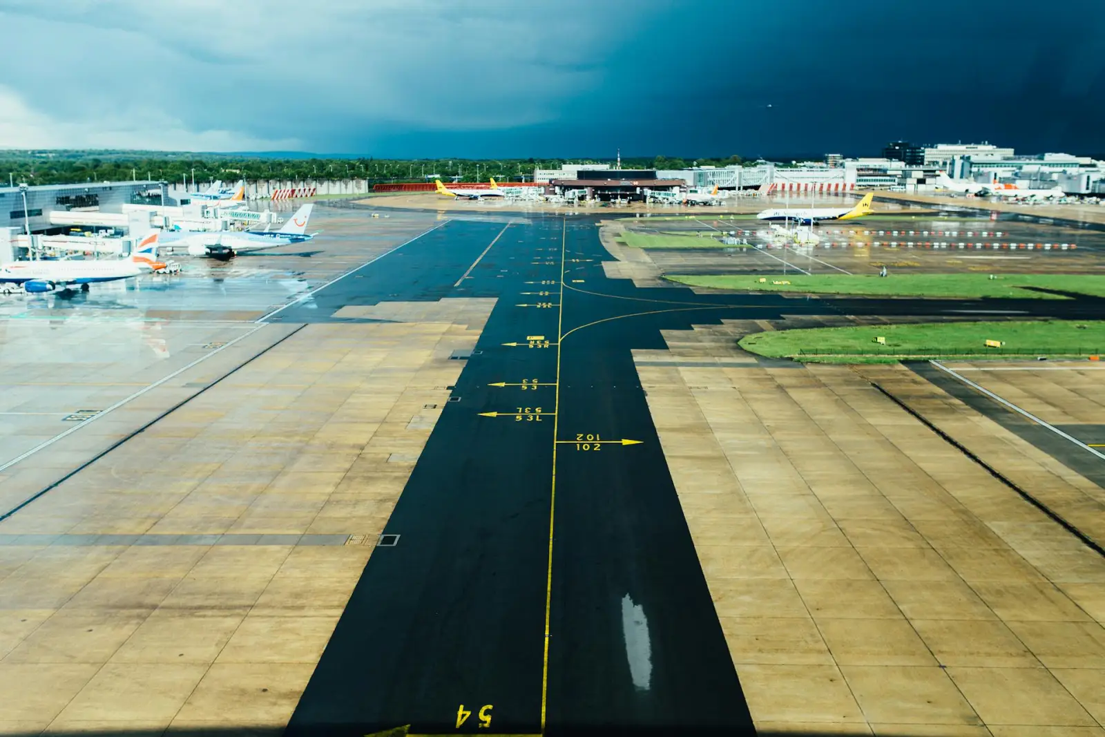 A wet airport runway with multiple parked airplanes and a stormy sky in the background.