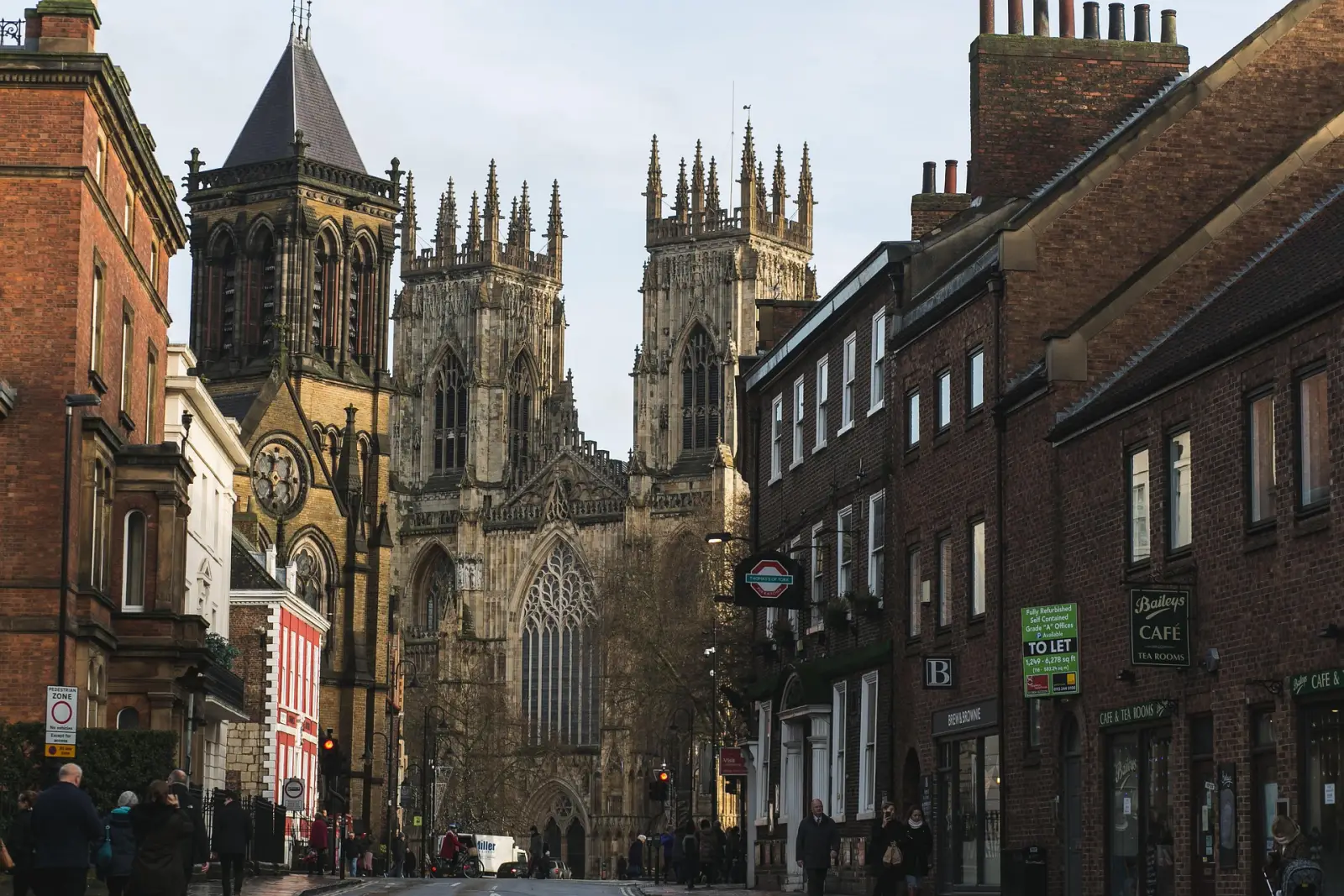 8 Of The Most Beautiful Places To Visit In England 2 Street view of York Minster, a stunning Gothic cathedral, with historic brick buildings lining the road in York, England.