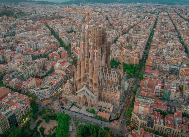 Spain Travel And Tourism News 9 An aerial photograph of the iconic Sagrada Família in Barcelona, showcasing its intricate spires and ongoing construction, framed by the city’s symmetrical grid layout. This architectural masterpiece by Antoni Gaudí is one of Spain’s most visited filming locations, featured in movies like Vicky Cristina Barcelona.