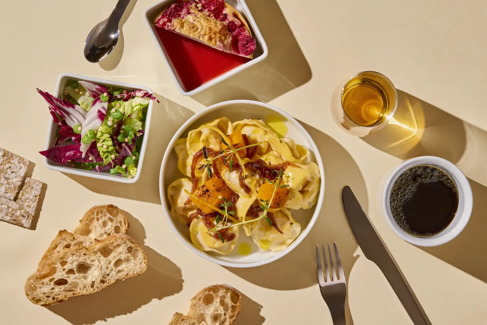 SAS airline food served onboard featuring tortellini with roasted vegetables, fresh salad, rye crispbread, dessert tart, coffee, and white wine.