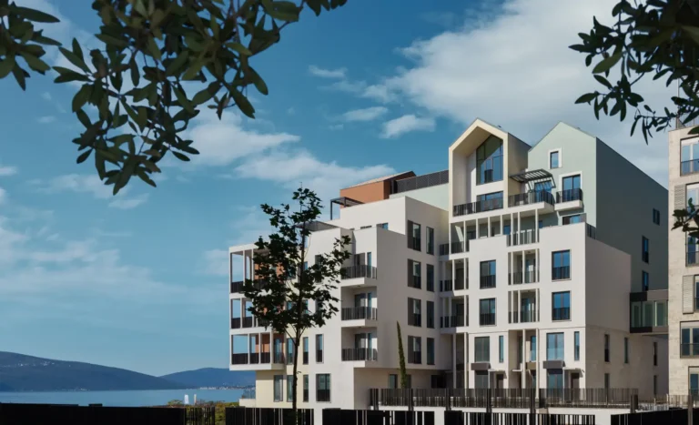Modern wellness hotel building with balconies overlooking the Adriatic Sea in Porto Montenegro, surrounded by blue skies and mountain views.