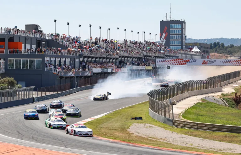 Nascar race cars speeding on the track at Circuit Ricardo Tormo with smoke rising and grandstands full of spectators in Valencia, Spain