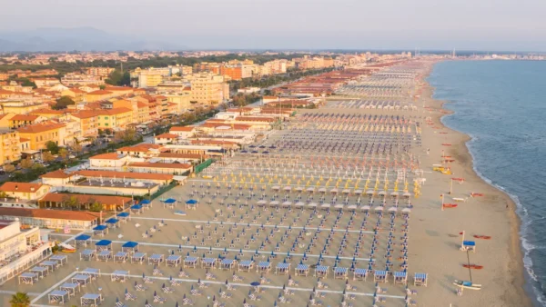 Private beach clubs with colorful umbrellas and sunbeds lined up along the sandy coast of Tuscany, Italy.