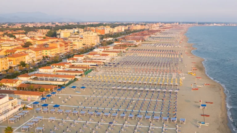 Private beach clubs with colorful umbrellas and sunbeds lined up along the sandy coast of Tuscany, Italy.