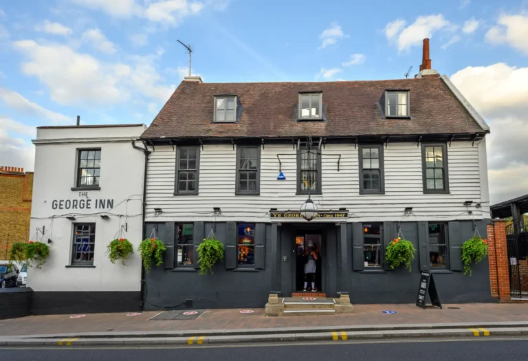 Historic façade of The George Inn pub in London, a 17th-century timber-framed coaching inn with hanging flower baskets and traditional signage.
