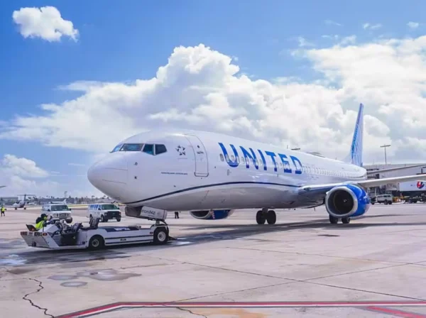 United Airlines Boeing 737-900 on the tarmac at LAX, connected to a ground vehicle under bright daylight.